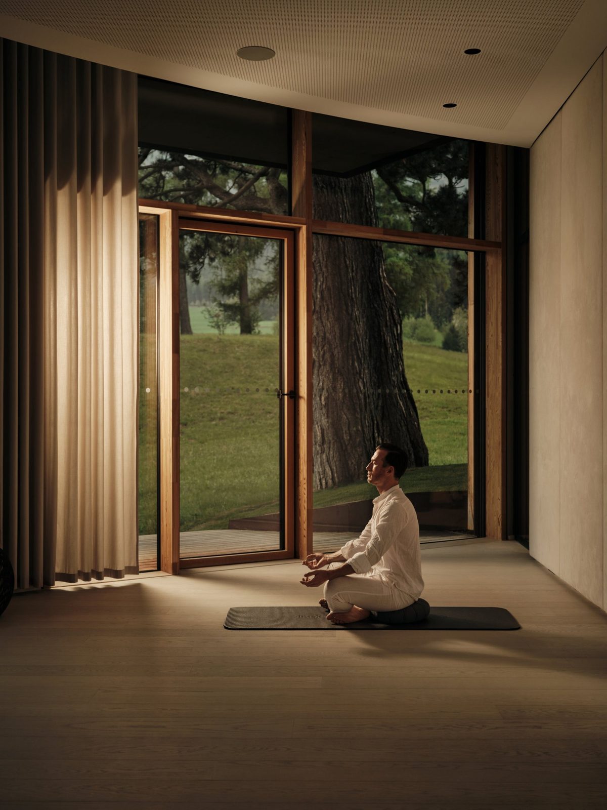A man meditating in a quiet, light-filled studio overlooking an ancient pine, Lanserhof