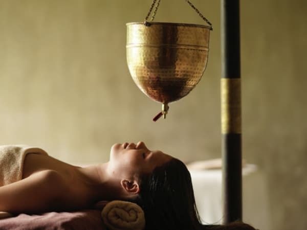 A guest receiving shirodhara, warm oil poured from a brass vessel, Santani Wellness